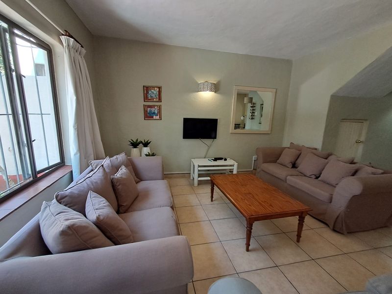 A comfortable living room featuring tiled flooring, neutral wall tones, and a window with security bars, providing a functional and well-lit space.