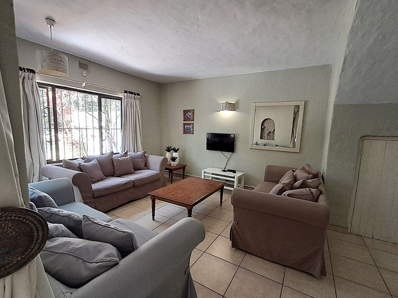 A comfortable living room featuring tiled flooring, security bars on the window, and wall-mounted lighting, offering a functional space for relaxation.