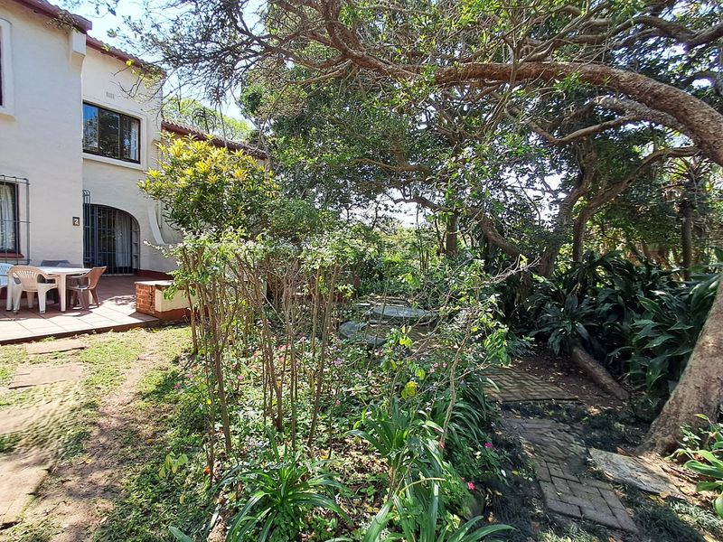A private rear garden featuring a tiled patio area, mature trees, and established landscaping with brick pathways.