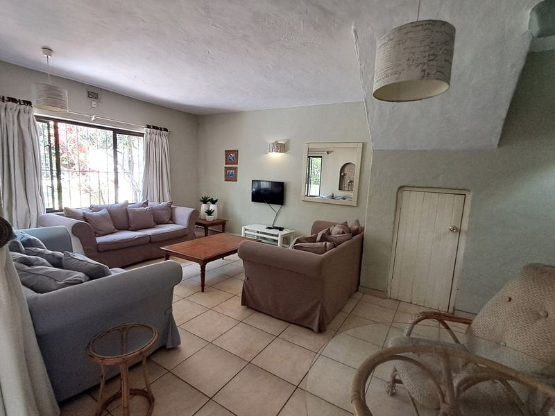 A spacious living room featuring tiled flooring, neutral walls, and a convenient built-in under-stair storage cupboard.