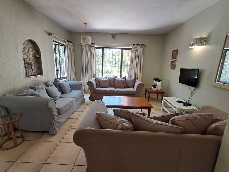 A comfortable living room featuring tiled flooring, an arched wall niche, and large windows with security bars, providing a functional and well-lit space.