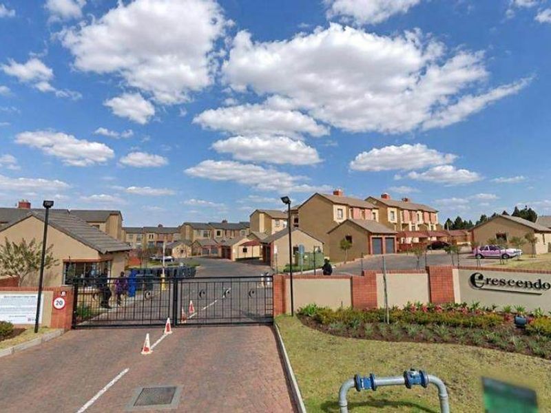 Street view of the Crescendo apartment complex entrance, featuring a secure gated access point, paved driveway, and established perimeter walling.