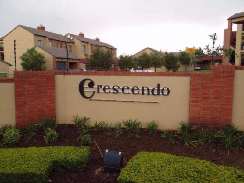 Entrance signage and landscaped garden area for the Crescendo apartment complex, featuring brick boundary walls and established greenery.