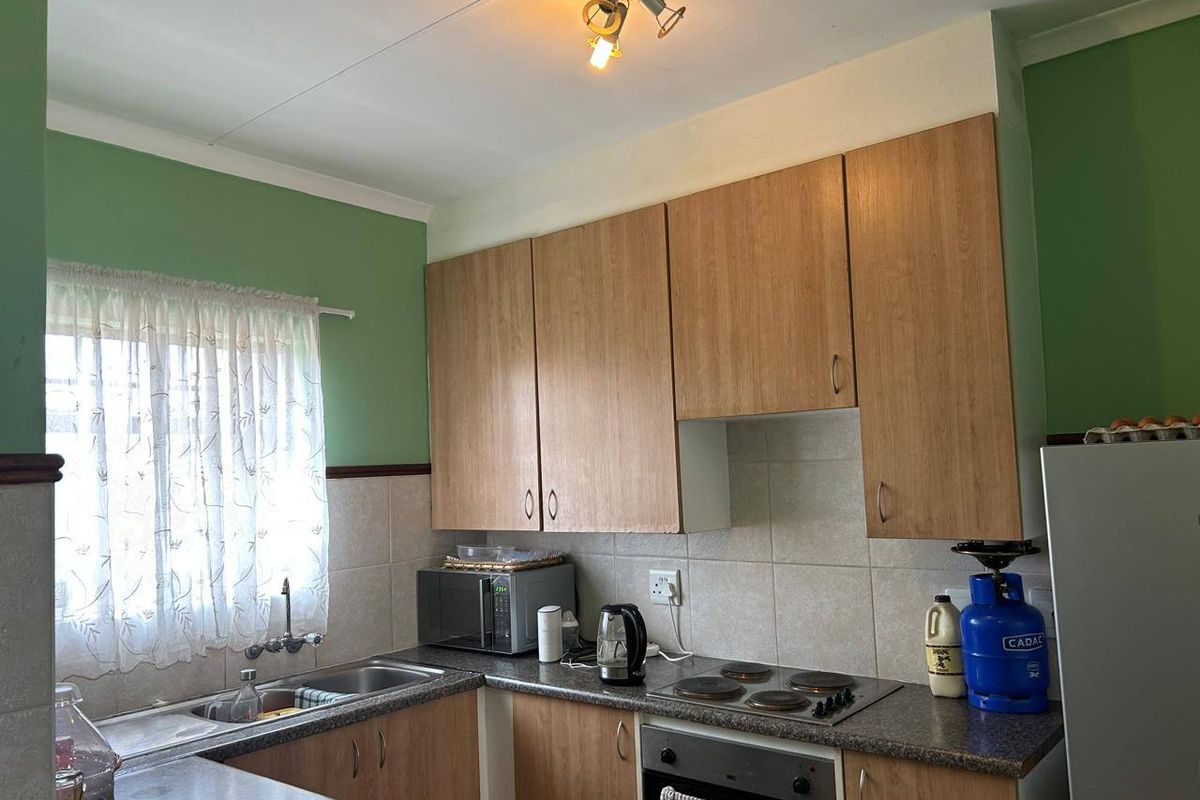 A functional kitchen featuring laminate cabinetry, a tiled backsplash, built-in oven and hob, and a stainless steel sink with a window view.