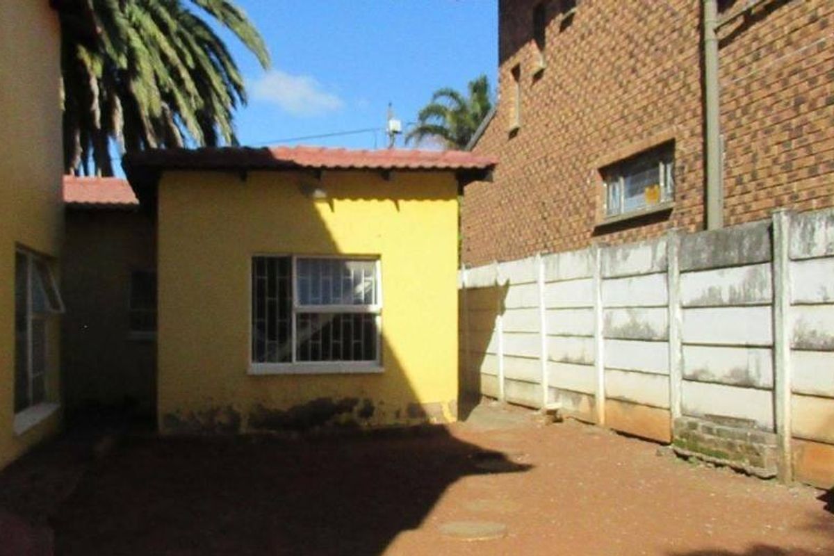 Rear exterior view of the property featuring a small yard area, precast concrete boundary wall, and yellow painted exterior walls with security bars.