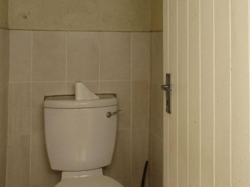 A small, dated bathroom featuring a standard toilet, tiled wall finishes, and timber paneling, currently in need of cosmetic updates.