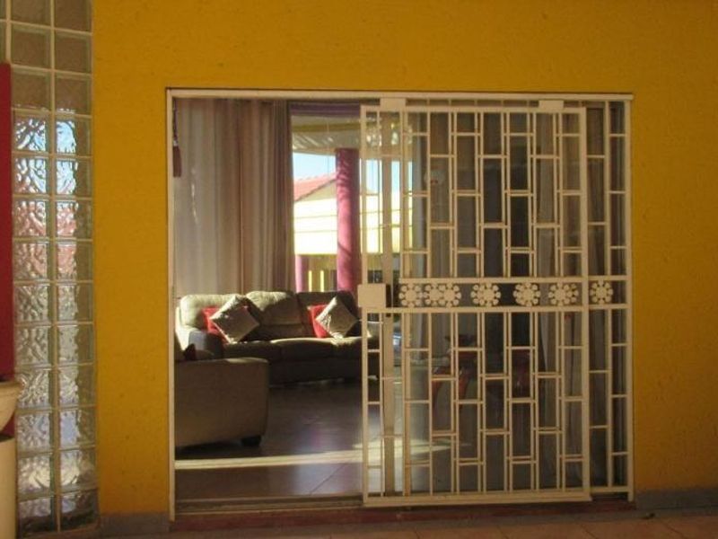 Covered patio area featuring a glass block feature wall, tiled flooring, and a security gate providing access to the interior living space.