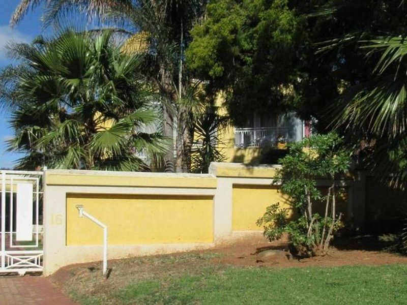 Front view of the property featuring a yellow boundary wall, metal driveway gate, and established garden area.