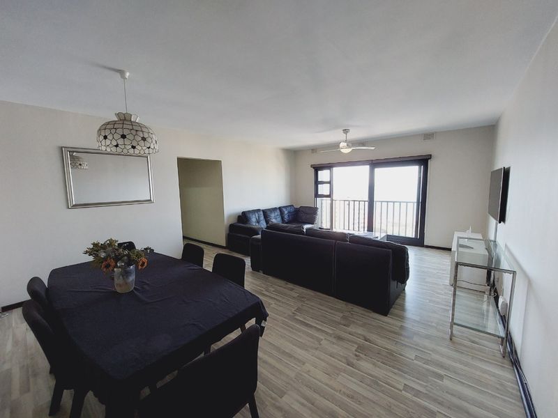 Spacious open-plan living and dining area featuring modern laminate flooring, a ceiling fan, and large sliding doors leading to a balcony.
