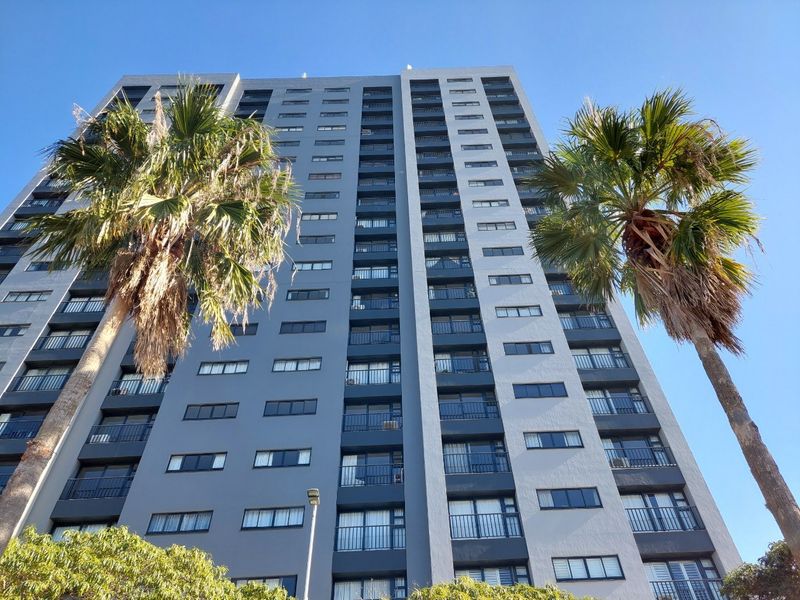 Low angle view of a high-rise apartment building facade featuring multiple balconies and large windows under a clear blue sky.