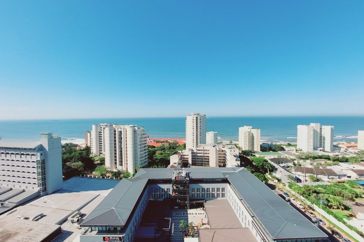 An elevated aerial view showcasing the surrounding urban landscape, nearby commercial buildings, and the coastal ocean horizon.