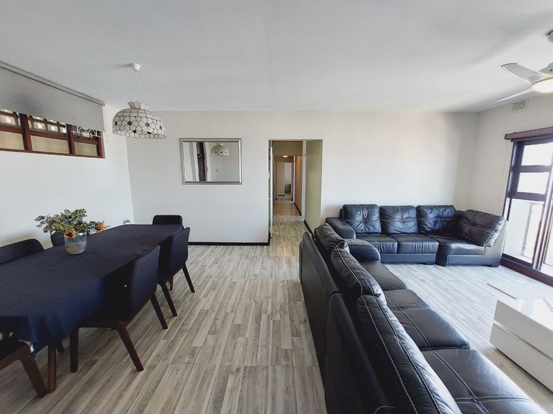 Spacious open-plan living and dining area featuring modern laminate flooring, a ceiling fan, and access to a balcony through sliding glass doors.