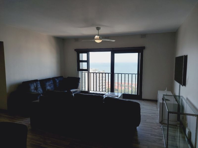 Living room featuring laminate flooring, a ceiling fan, and large sliding glass doors opening onto a balcony with ocean views.