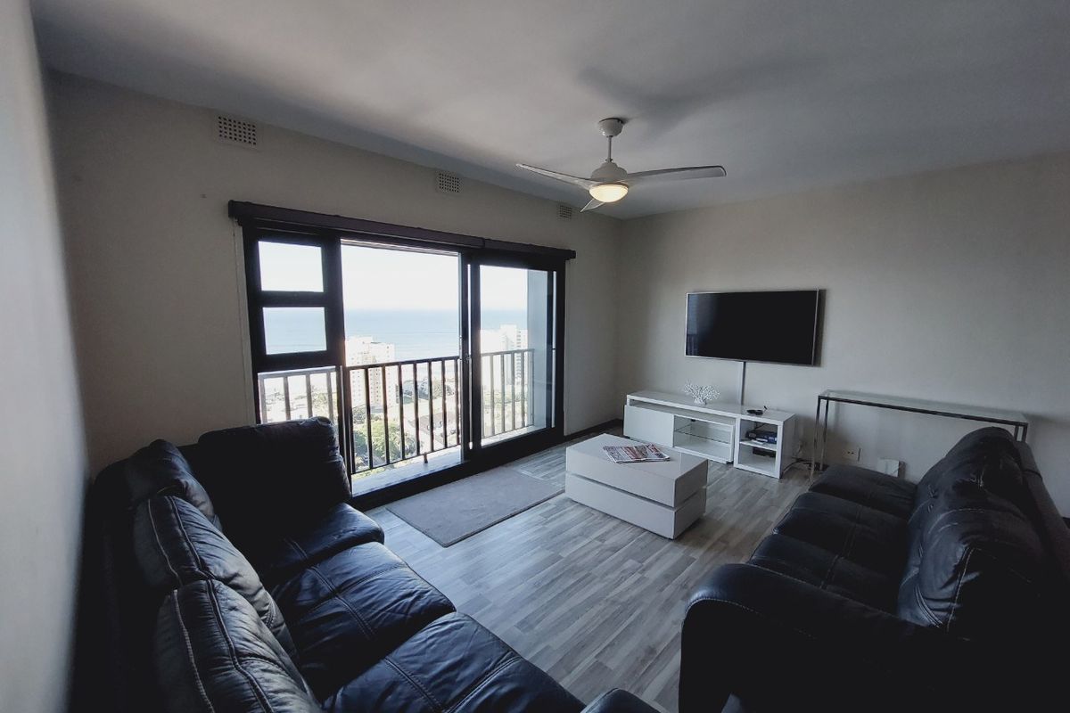 A comfortable living room featuring laminate flooring, a ceiling fan, and large sliding glass doors that open to a balcony with ocean views.
