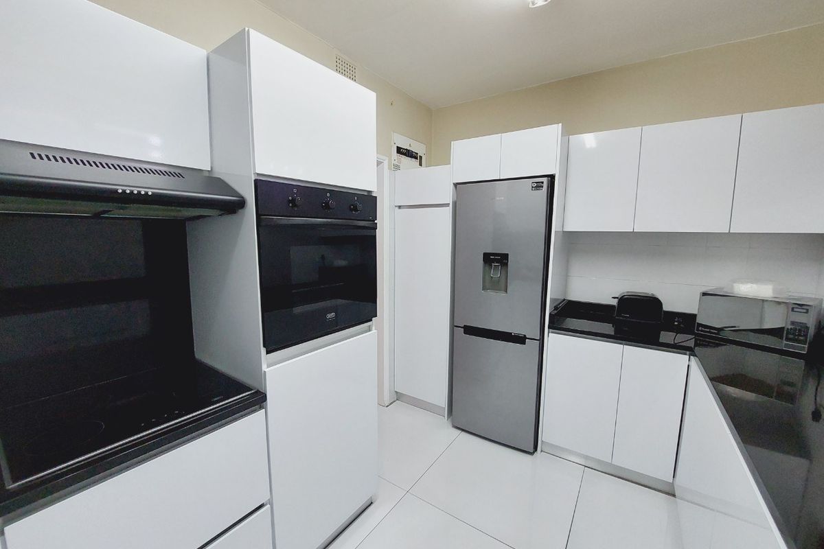 Modern kitchen featuring sleek white cabinetry, black granite countertops, built-in oven, extractor fan, and tiled flooring.