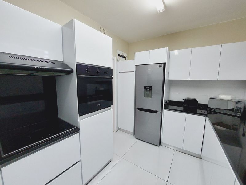 Modern kitchen featuring sleek white cabinetry, black granite countertops, built-in oven, extractor fan, and tiled flooring.