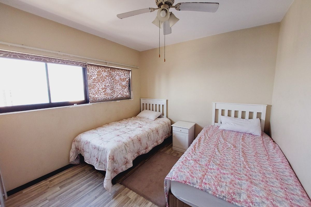 A functional bedroom featuring laminate flooring, a ceiling fan, and a large sliding window providing natural light.
