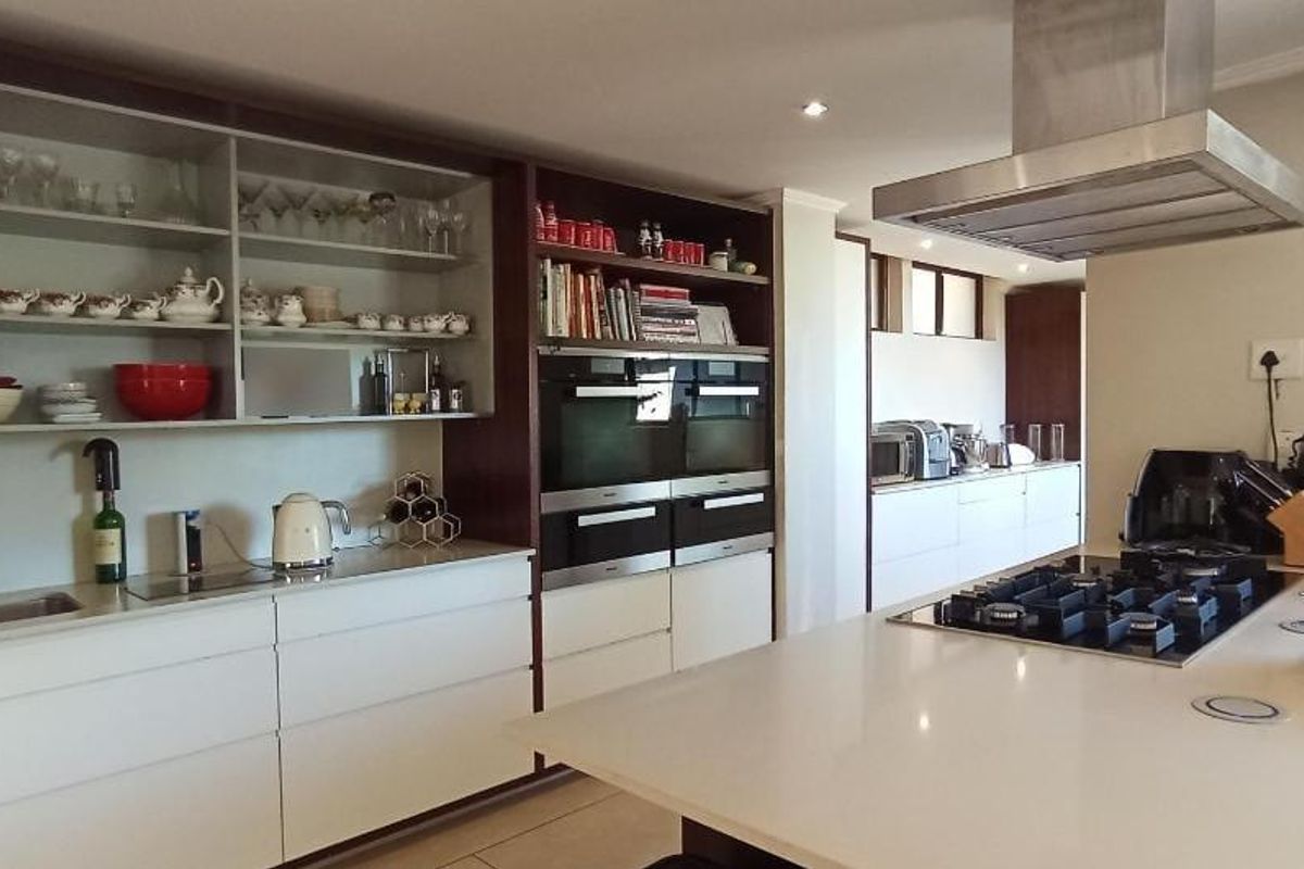 Modern kitchen featuring extensive built-in cabinetry, stone countertops, a central island with a gas hob, and integrated double wall ovens.
