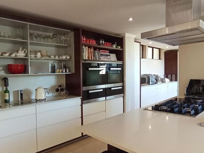 Modern kitchen featuring extensive built-in cabinetry, stone countertops, a central island with a gas hob, and integrated double wall ovens.