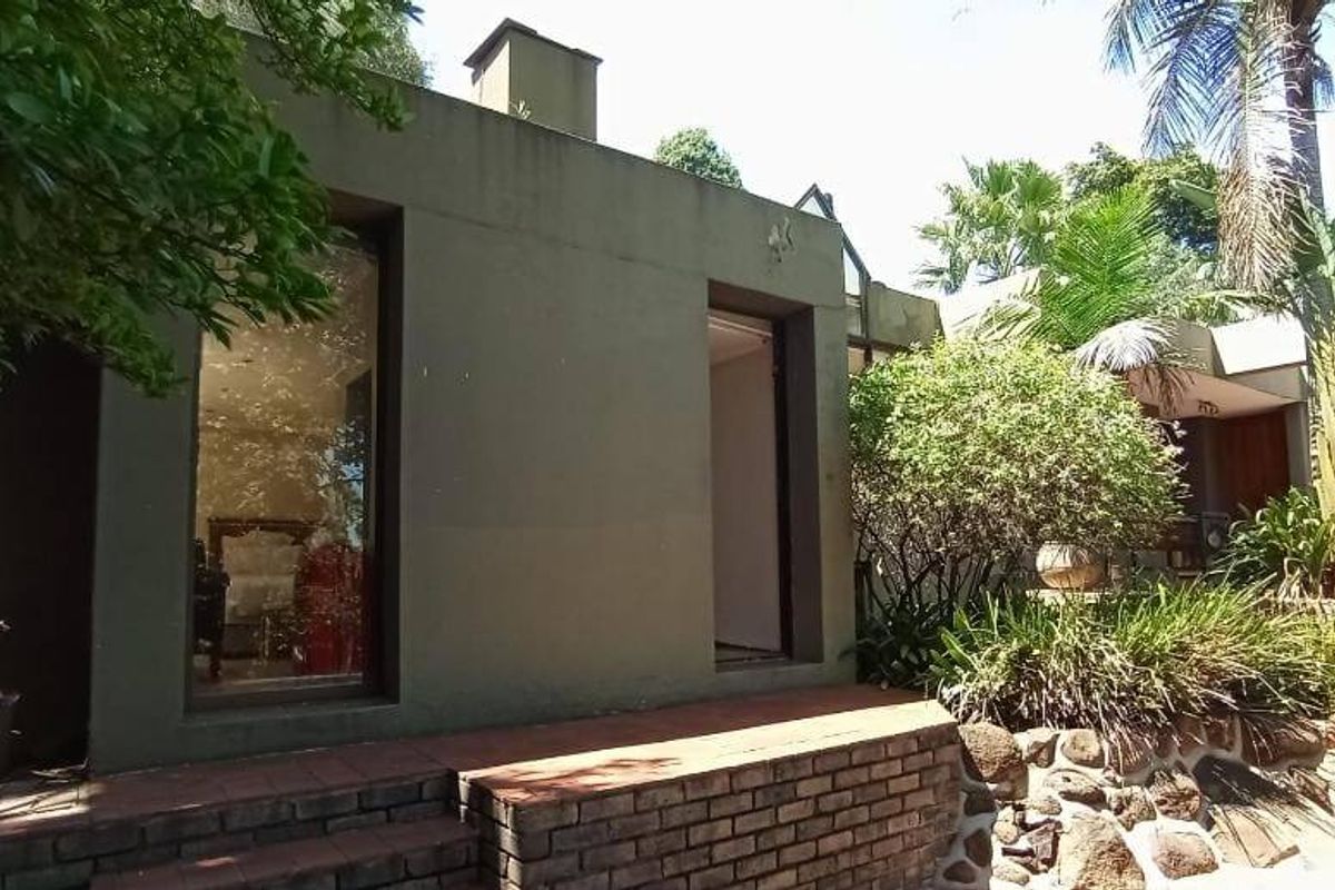 A rear exterior view of the property featuring a brick retaining wall, paved patio space, and large windows looking into the home.