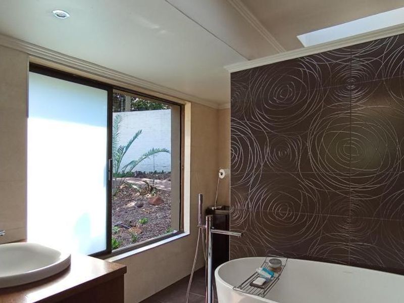 Modern bathroom featuring a freestanding bathtub, decorative feature wall tiling, a vessel sink vanity, and a skylight providing natural light.
