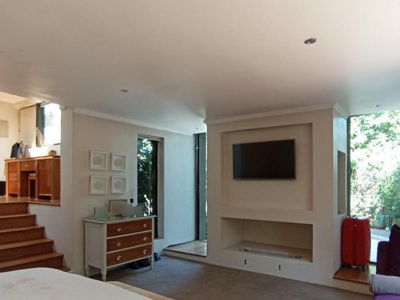 Spacious bedroom featuring a built-in fireplace, recessed television niche, and a timber staircase leading to an elevated area with direct garden access.