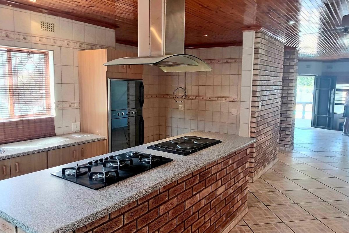 Spacious kitchen featuring a brick island with dual hobs, built-in oven, stainless steel extractor, and timber ceiling, offering a functional layout ready for modernization.