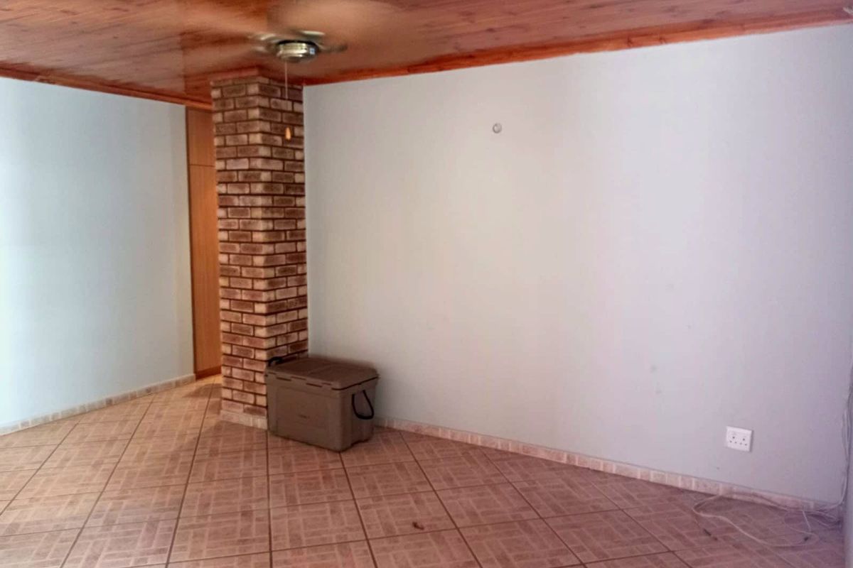 A spacious living area featuring a distinctive exposed brick pillar, timber ceiling, and ceramic tiled flooring, offering a blank canvas for interior design.