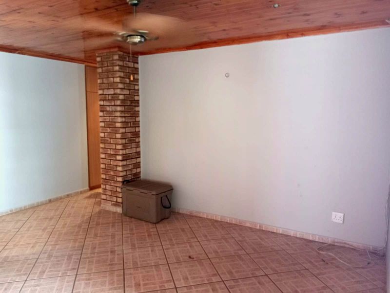 A spacious living area featuring a distinctive exposed brick pillar, timber ceiling, and ceramic tiled flooring, offering a blank canvas for interior design.