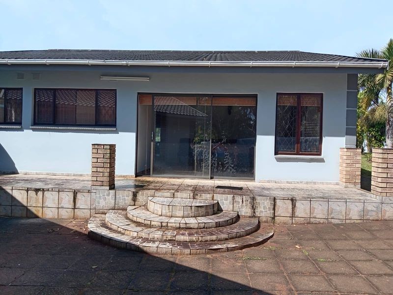 Rear exterior view of the house featuring a tiled patio, brick pillars, and sliding glass door access to the interior.