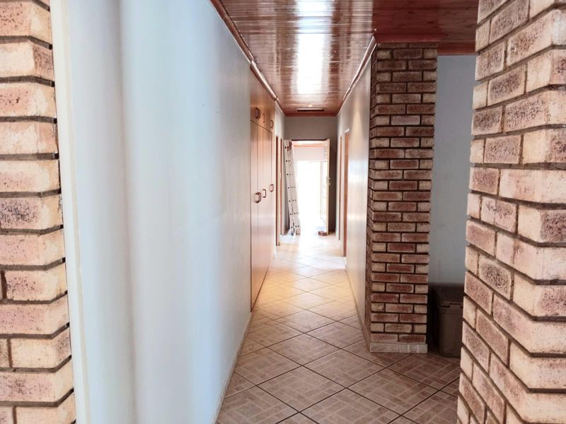 A spacious hallway featuring tiled flooring, built-in storage cupboards, and a distinctive timber ceiling with an exposed brick structural pillar.