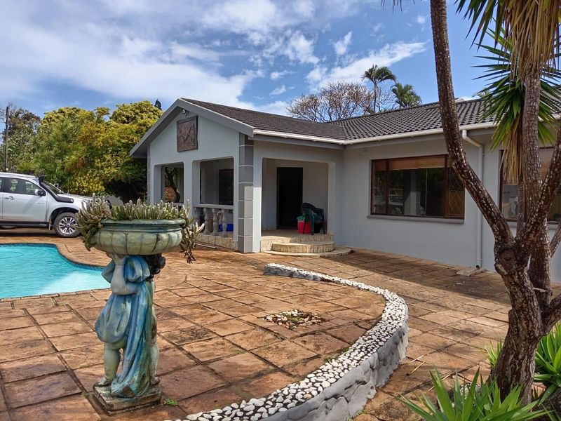 Rear exterior view of the house featuring a swimming pool, a spacious tiled patio area, and a stone-clad retaining wall.