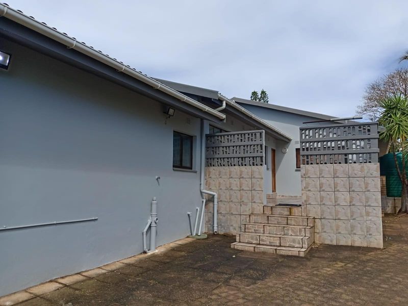 Rear exterior view of the property featuring a paved courtyard, tiled steps, and decorative breeze block privacy screens.