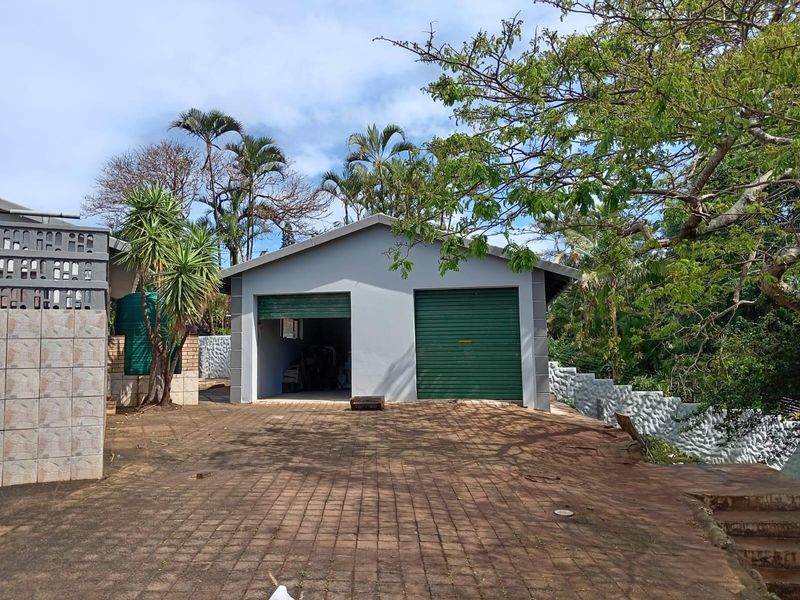 A detached double garage featuring roller shutter doors, situated on a paved driveway with surrounding landscaped garden and retaining walls.