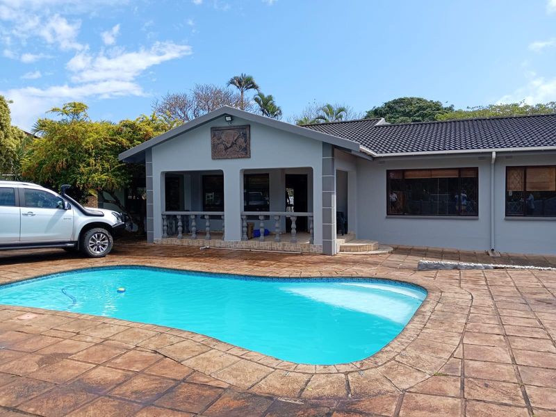 Exterior view of a residential property featuring a swimming pool, paved pool deck, and a covered patio area with balustrades.