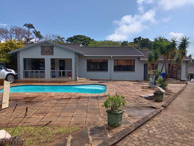 Rear view of the house featuring a swimming pool, covered veranda with concrete balustrades, and extensive paved outdoor entertainment area.