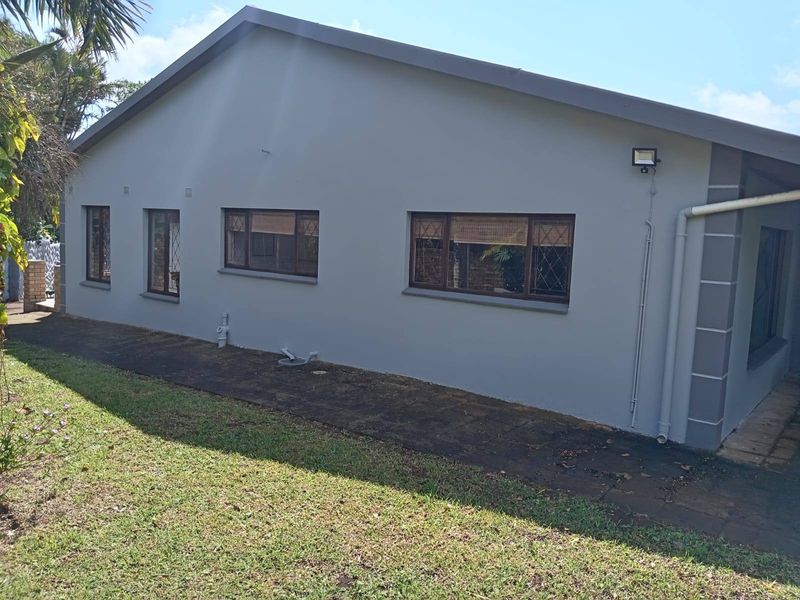Rear exterior view of the house featuring a paved walkway, security lighting, and diamond-pattern window grilles along the side wall.