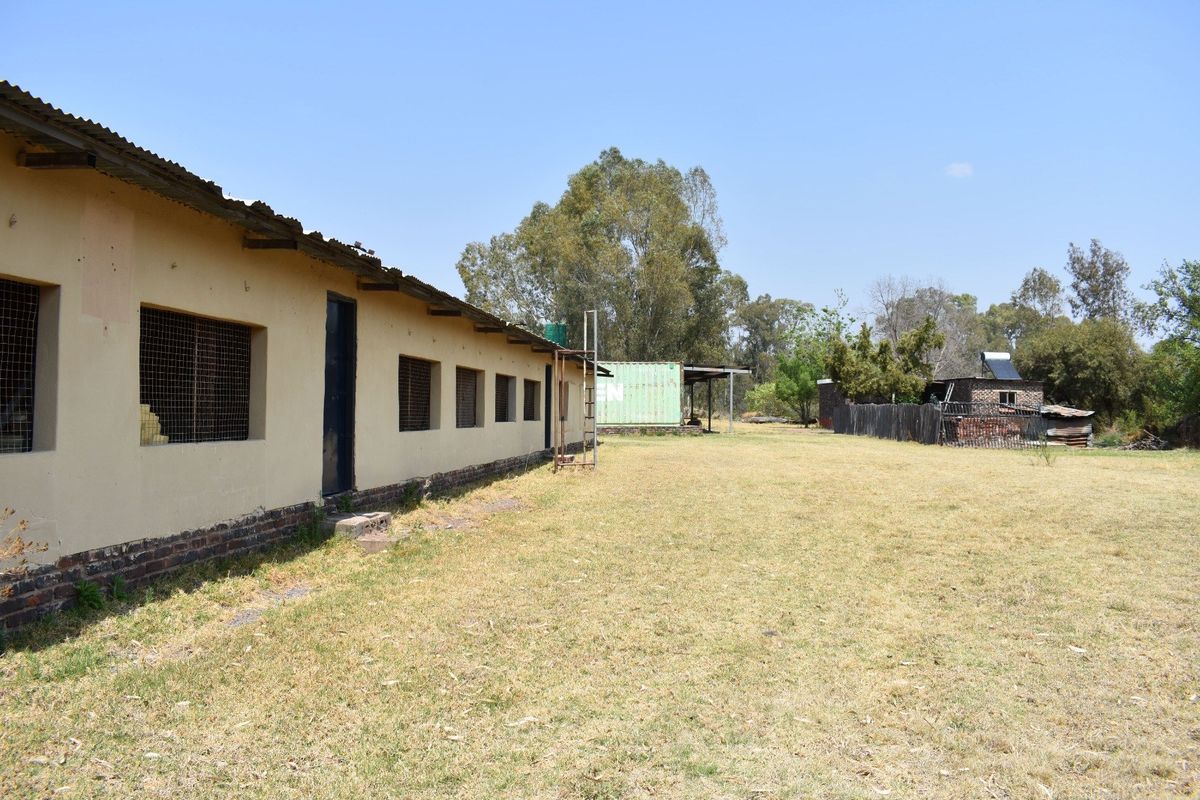 Rear view of a farm building featuring a corrugated metal roof, brick foundation, and security mesh window screens set on a large open plot.