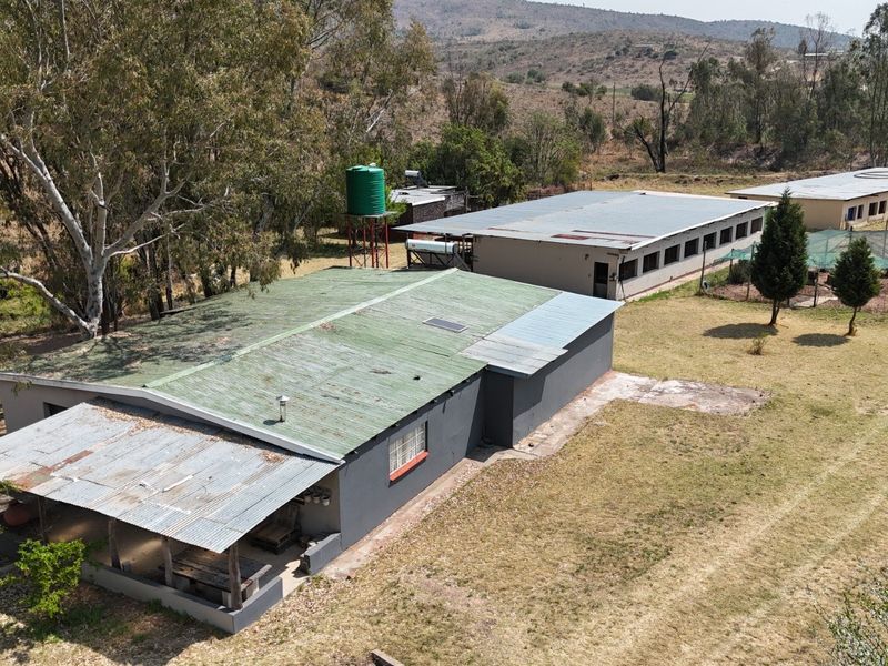 Aerial view of a farm property featuring multiple outbuildings, corrugated metal roofing, a water storage tank, and a covered patio area.