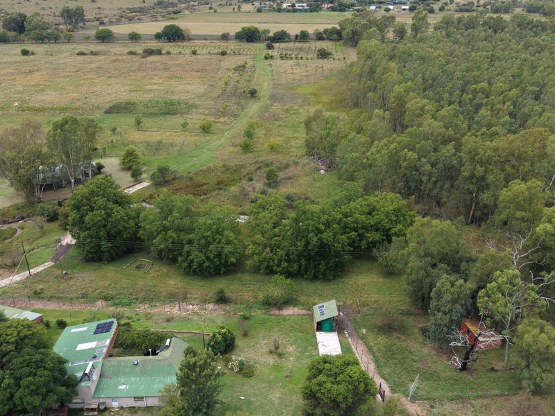 Aerial view of the farm property showcasing the main dwelling with solar panels, surrounding outbuildings, expansive grounds, and established tree lines.