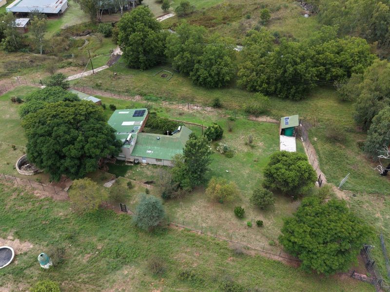 Aerial view of the farm property featuring the main dwelling with solar panels, surrounding garden, outbuildings, and extensive fenced grounds.