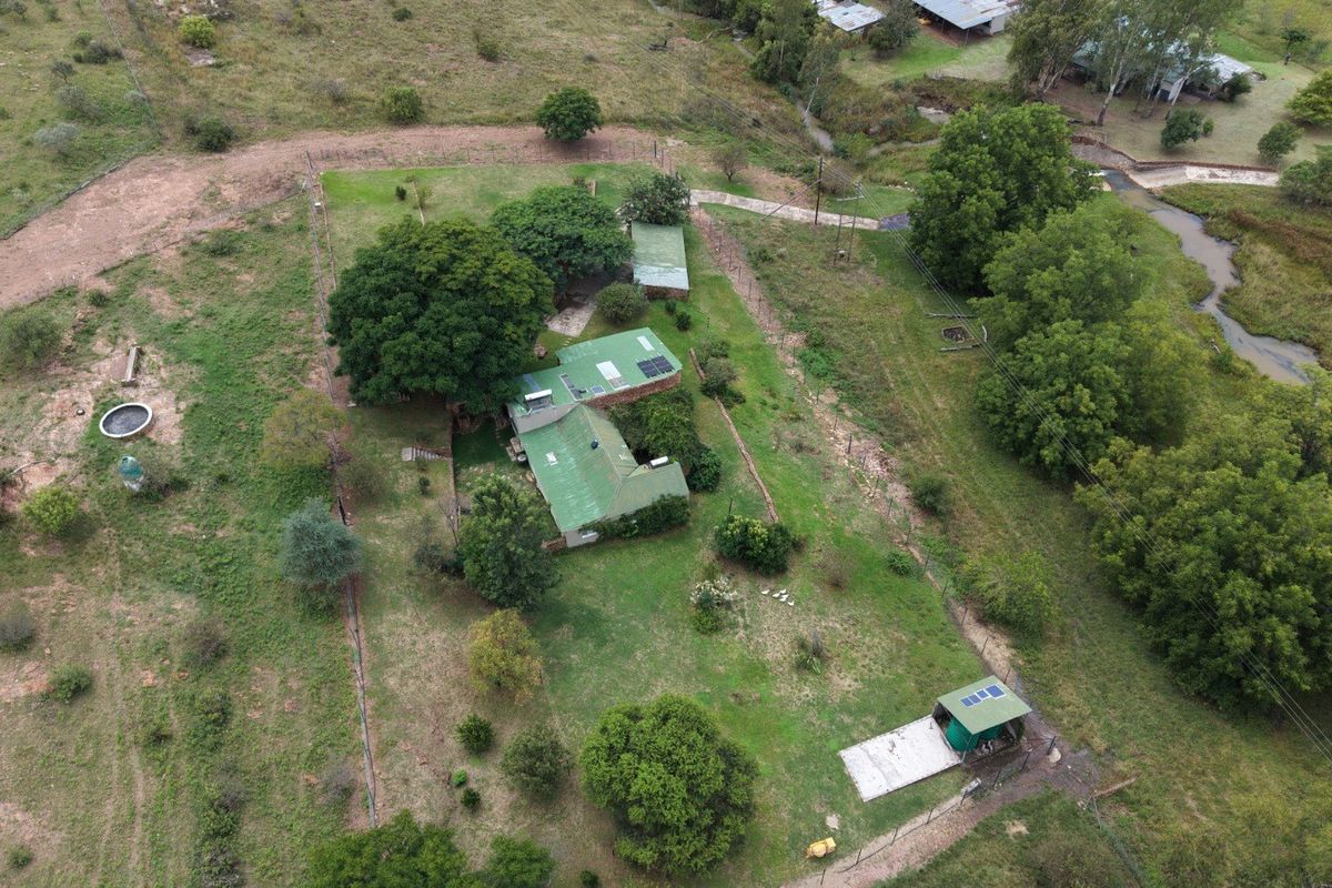 Aerial view of a rural farm property featuring multiple structures with green metal roofing, solar installations, and surrounding fenced grounds.