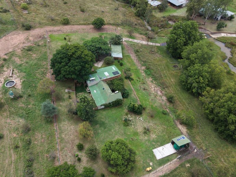 Aerial view of a rural farm property featuring multiple structures with green metal roofing, solar installations, and surrounding fenced grounds.