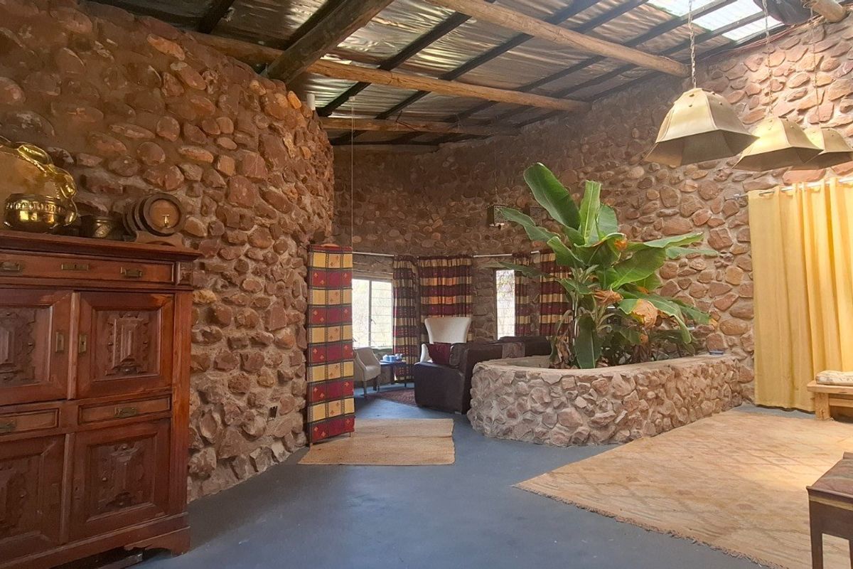 Spacious living area featuring rustic exposed stone walls, a high timber-beamed ceiling with skylights, and a unique built-in stone planter.