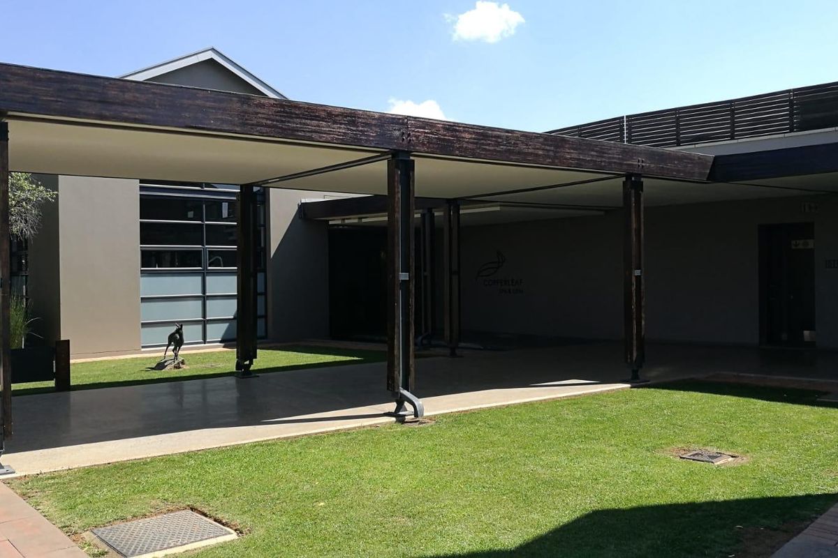A spacious covered patio area featuring timber support beams and paved flooring, overlooking a well-maintained lawn.