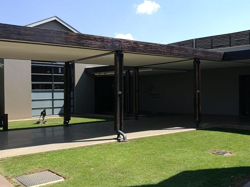 A spacious covered patio area featuring timber support beams and paved flooring, overlooking a well-maintained lawn.
