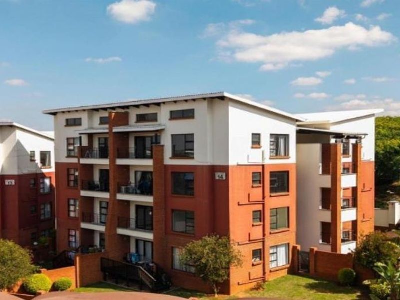 A view of a modern multi-story apartment complex featuring brick and white facade finishes, private balconies, and established landscaped grounds with covered parking.