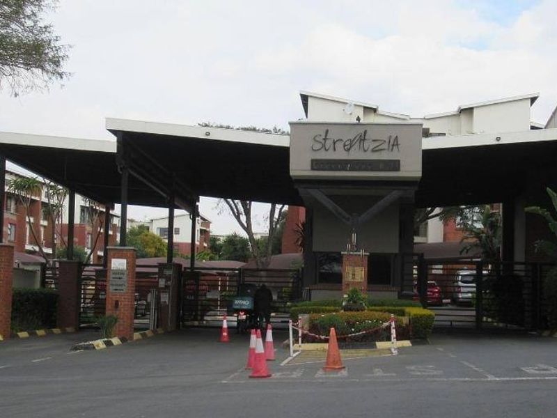 The main entrance and security gatehouse of the Strelitzia apartment complex, featuring brick masonry and a covered access point.