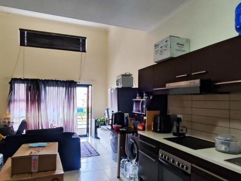 Open-plan living area featuring a modern kitchen with dark cabinetry, electric hob, and tiled flooring, leading to a balcony through a sliding door.