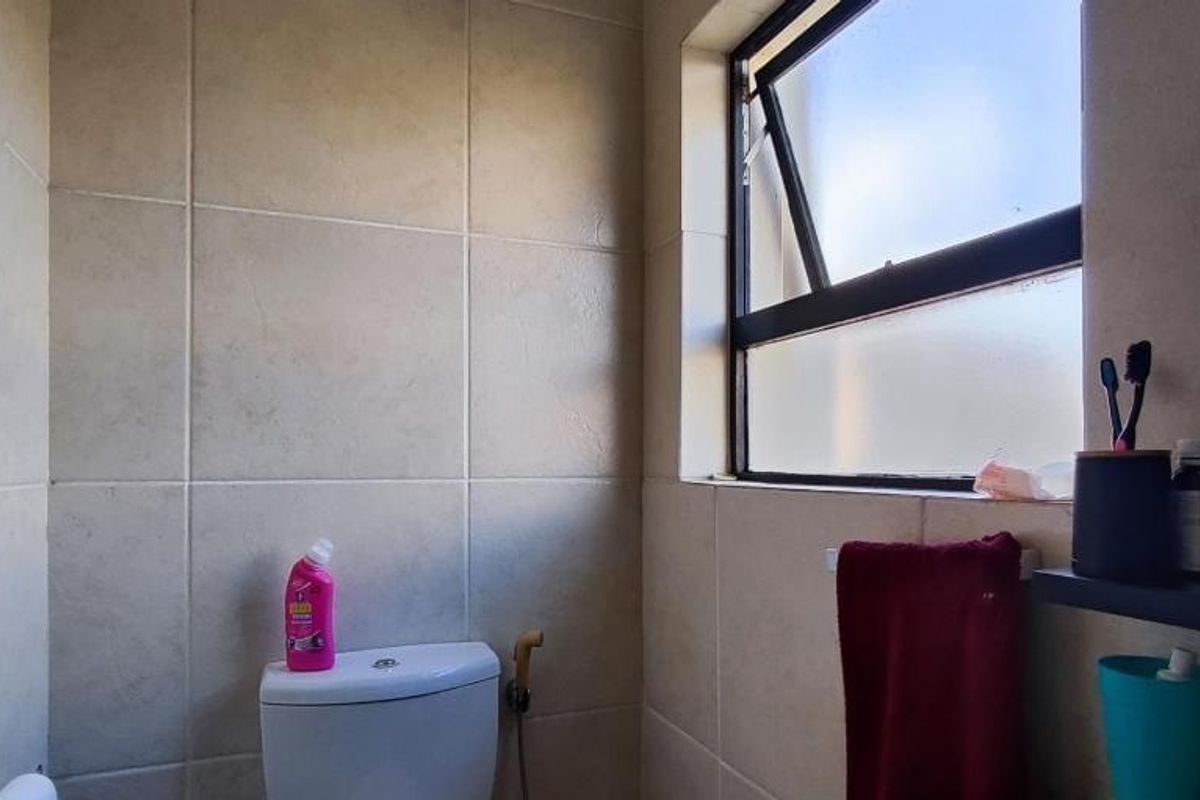 A functional bathroom featuring tiled walls, a standard toilet with a bidet spray, and a top-hung window for ventilation.